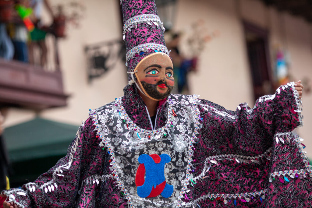 A man dressed in a colourful costume with a bearded mask covering his face on parade in the Cajamarca Carnival