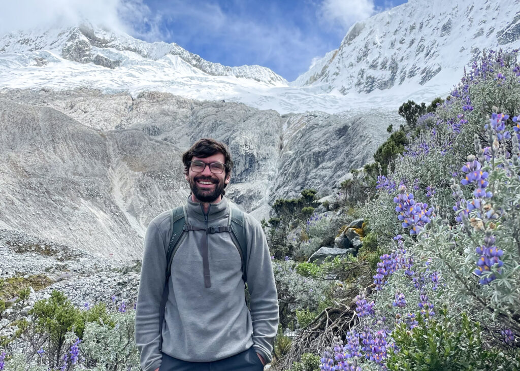 Dan with his hiking backpack on with snow-capped mountains behind on the hike to Laguna 69. 