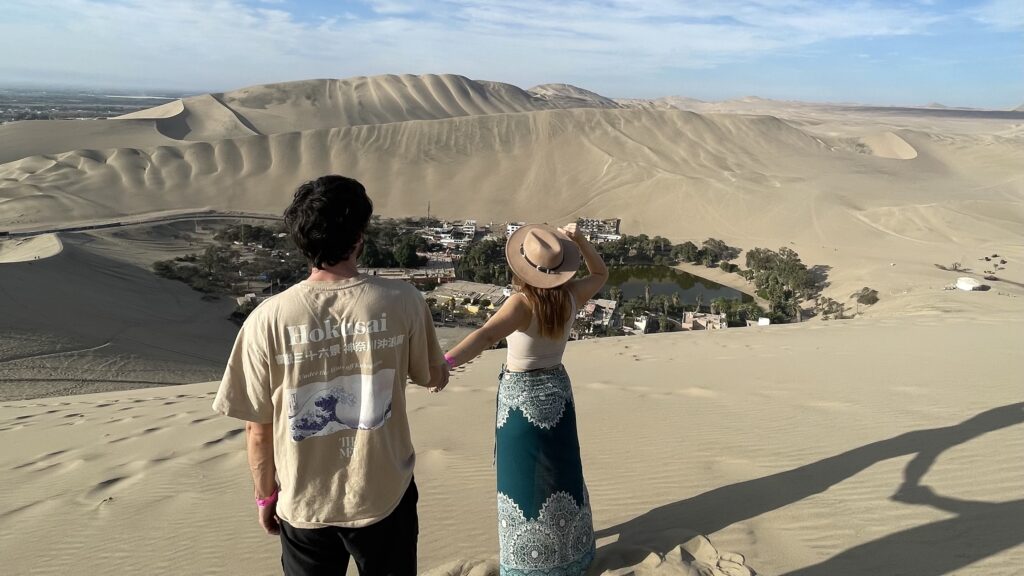 Megan and Dan stood on a sand dune looking down at Huacachina desert oasis.