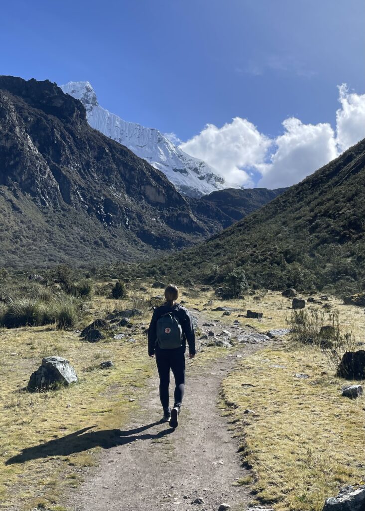 Megan walking through the valley with mountains on either side at the start of the Laguna 69 hike