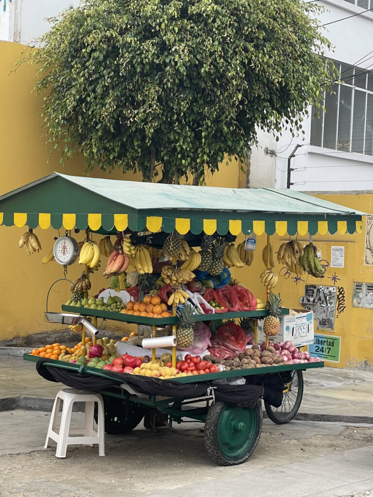 Cute fruit stall on the street in Lima with bananas hanging from the top and a variety of fruit around the edges 