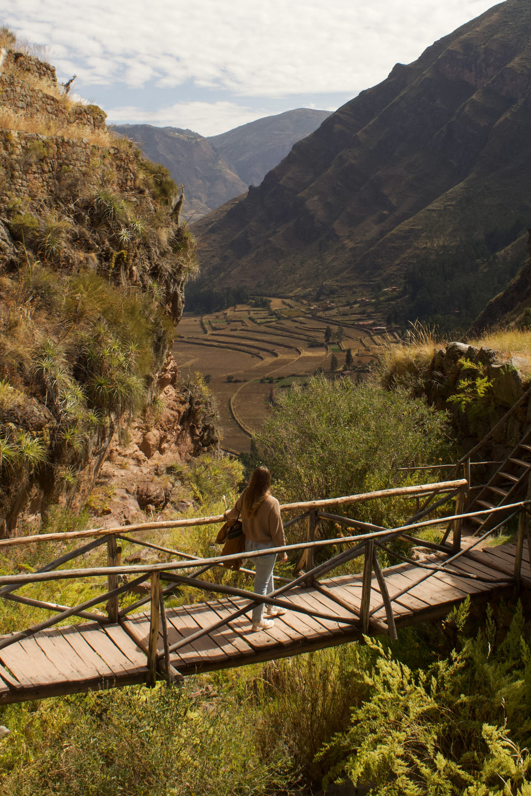 Megan walking across a wooden bridge looking over the Sacred Valley on the hike down from the Pisac Ruins.